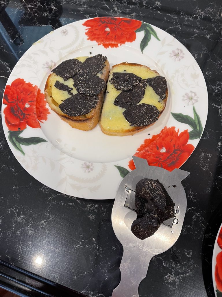 A cheese toast with shaved truffle on top. A truffle grater with some extra shaved truffle on the side.